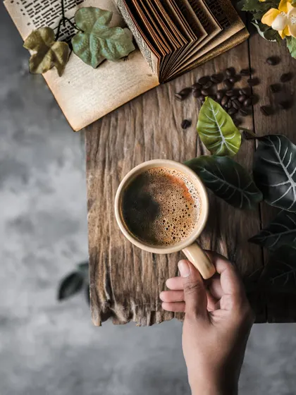 A hand holding a cup of coffee, adding a human touch to the reflective coffee flatlay scene.