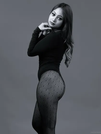 A black and white portrait of a model in a bodysuit and patterned stockings, with a soft and elegant pose.