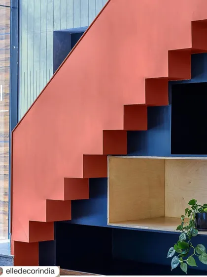 A close-up of the architectural staircase, showing how its strong color and form act as a sculptural element within the space. The built-in shelving underneath provides a clever and aesthetic storage solution.
