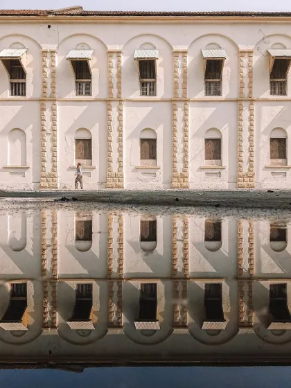 A creative composition showing a building and its perfect reflection in a puddle. A person walking by is also reflected, creating a symmetrical and surreal image that plays with perception.