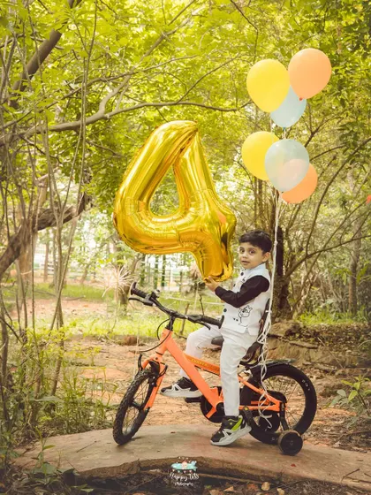 A birthday boy with his bike and a giant number '4' balloon. This outdoor setting allows for creative and celebratory birthday photos.