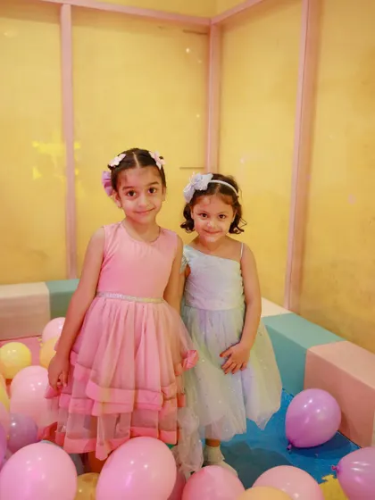 Two little princesses enjoying a magical birthday party, complete with beautiful dresses and a balloon-filled play area.