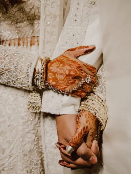 A close-up on the hands, a simple yet powerful symbol of their union. The bride's intricate henna and bangles contrast with the groom's simple hold, telling a story of two lives joining as one.