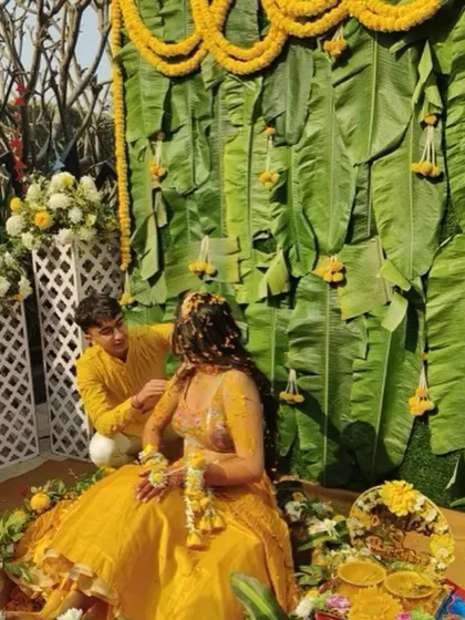 A classic Haldi moment with a backdrop of fresh banana leaves and marigold garlands. The bride, dressed in yellow, is seated for the rituals, creating a picture of tradition and joy.
