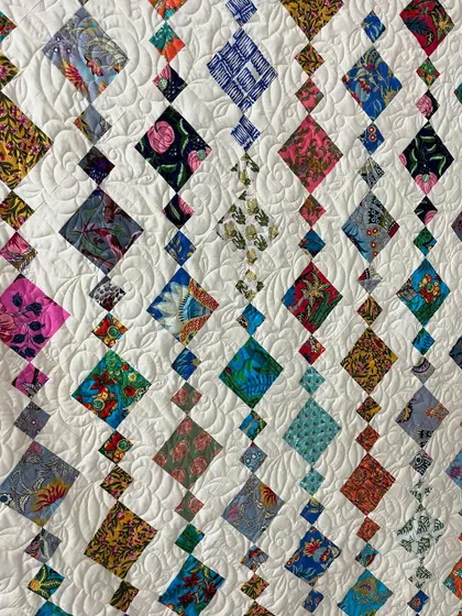 A detailed view of a "Chandelier" quilt, with a swirling feather quilting pattern in the background.