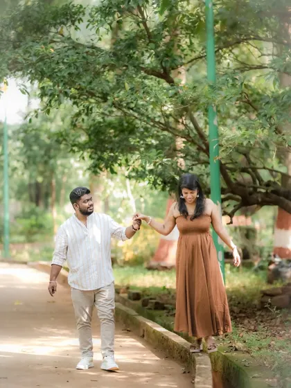 A playful and candid shot of a couple walking in a park, with the bride balancing on a ledge while holding her partner's hand. This captures their fun-loving dynamic.