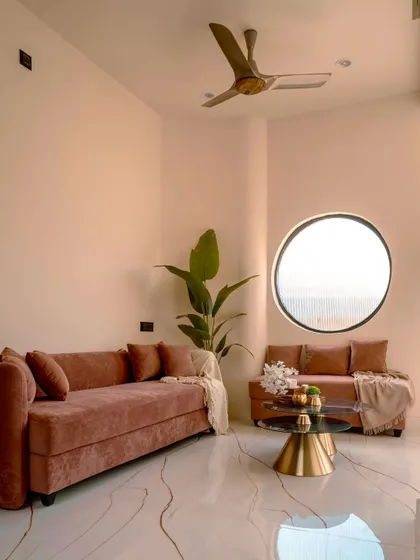 A cozy family lounge area in the 'Sukoon' home, featuring plush pink sofas and a distinctive circular window that frames the view outside.