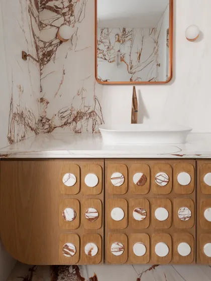 A powder room that makes a statement with dramatic red-veined white marble wrapping the walls and floor. We designed a custom wood veneer vanity with unique marble-inlaid circular details on the drawers.