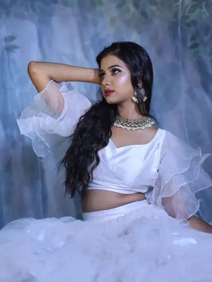 A serene and angelic portrait of a model in a white ruffled outfit, posing against a soft blue-grey background.