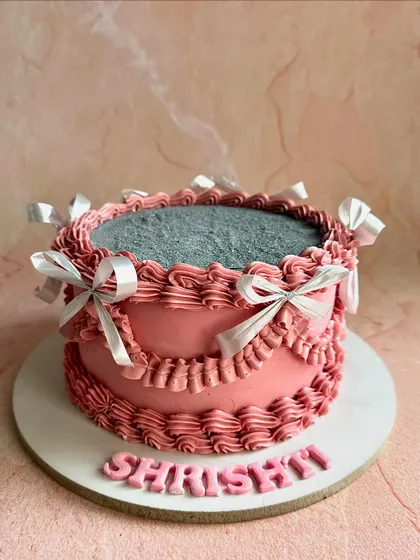 This personalized vintage cake for "Shrishti" features delicate pink piping, silver satin bows, and a glittering top, combining classic techniques with a touch of modern sparkle.