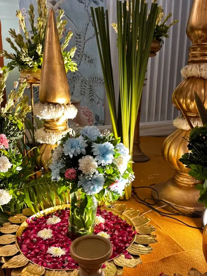A detail shot of the decor for a spiritual gathering, featuring a traditional brass 'urli' filled with water and flower petals, surrounded by floral arrangements.