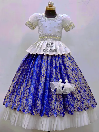An elegant white and royal blue Banarasi lehenga. The white peplum top is paired with a skirt that has a double-layered hem, adding volume and a touch of modern design.