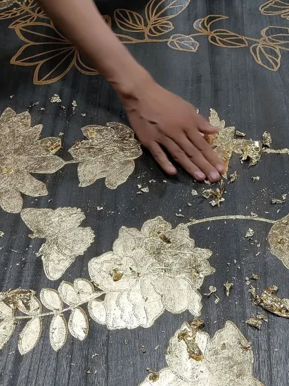 An artisan meticulously applies gold leaf to the laser-cut 'Flourish' wallcovering. This behind-the-scenes shot showcases the state-of-the-art technology and handcrafted care that go into creating these remarkable murals.
