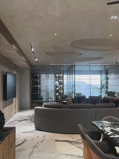 The expansive living area in this modern home is defined by its curved sofa and dramatic marble flooring. The design uses recessed ceiling details and track lighting to create a sense of volume and intimacy.