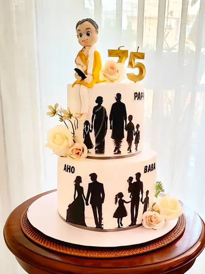 A grand two-tier cake celebrating a 75th birthday, decorated with family silhouettes that tell the story of a growing family. A custom fondant figure sits on top, representing the patriarch.
