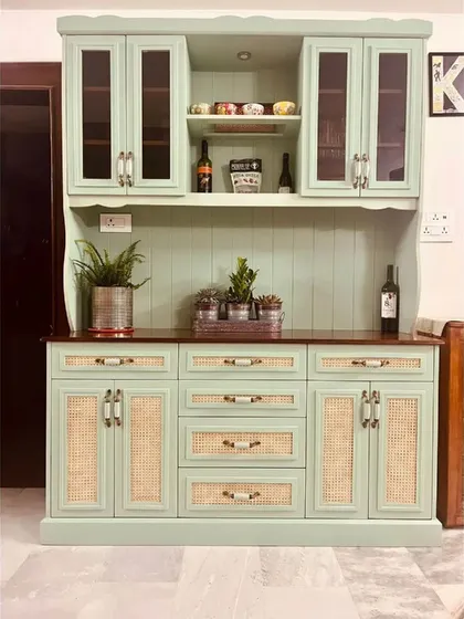 This magnificent hutch cabinet is a perfect blend of farmhouse style and modern needs. Finished in a soft sage green, it features glass-fronted cabinets, open shelving, wine storage, and drawers with rattan accents.