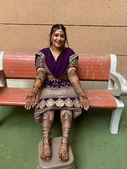 A beautiful bride in her traditional purple outfit, showcasing her complete bridal mehandi on both hands and feet. The intricate designs are perfect for her wedding day.