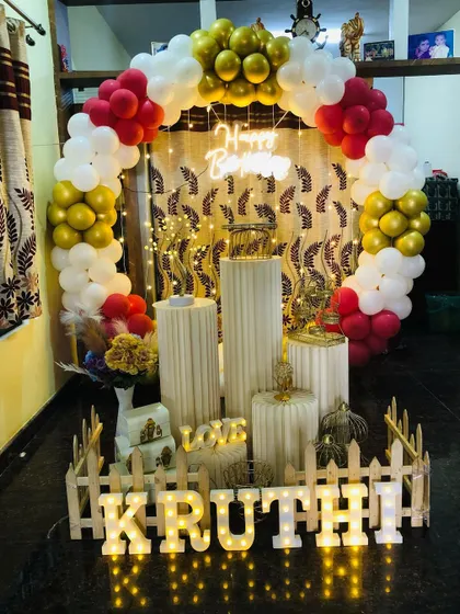 A simple and classic birthday decoration with red, white, and gold balloons. This setup includes the full prop display with a picket fence and marquee letters.