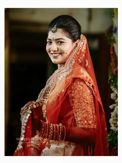 A smiling bride in her beautiful red and gold wedding attire, looking radiant and ready for her ceremony.