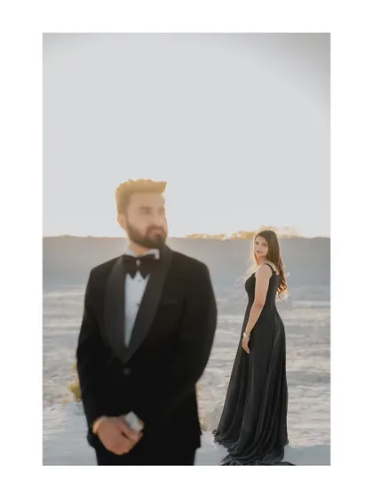 A stylish portrait with a focus on the groom in his sharp tuxedo, while the bride stands elegantly in the background. This composition creates a sense of drama and sophistication.