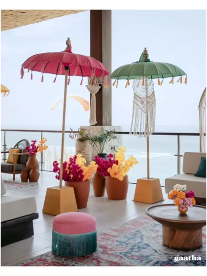 A closer look at the vibrant decor, showing the mix of pink and green Balinese umbrellas, fringed ottomans, and colorful floral arrangements.