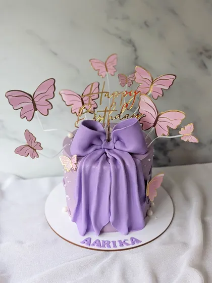 The trending bow cake, made for my own baby girl. This purple cake is designed to look like a gift, with a large fondant bow and a flight of butterflies.