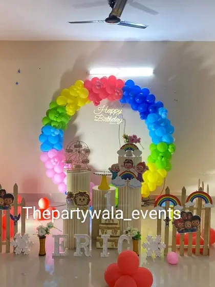 A colorful Cocomelon party with a rainbow balloon ring and character cutouts.