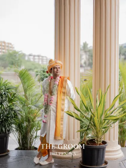 A stylish portrait of the groom leaning against a pillar, looking confident and happy on his wedding day.