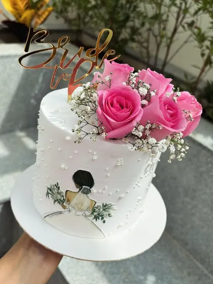A beautiful cake for a bride-to-be. The design includes an illustration of a bride, delicate pearl sprinkles, and a bouquet of fresh pink roses.