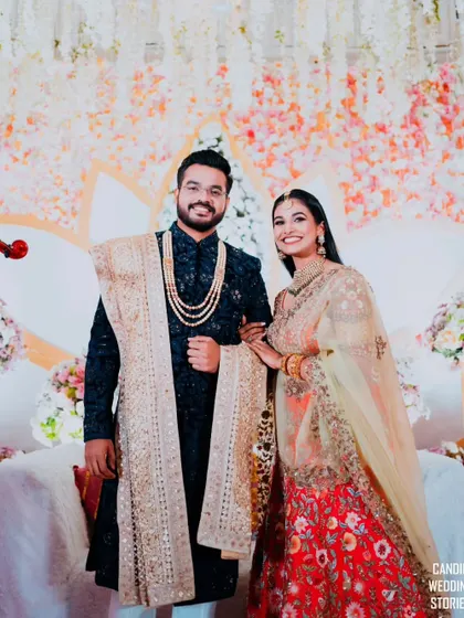 The couple posing on their reception stage, framed by a beautiful floral backdrop, a perfect memory of their celebration.