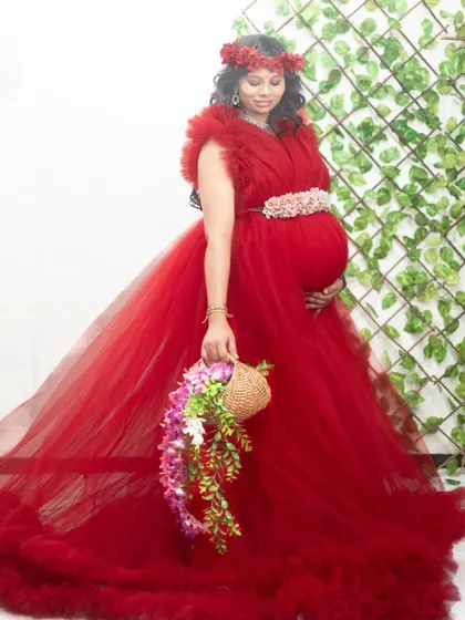 A beautiful mom-to-be in our red ruffle gown, accessorized with a floral crown and belt for a boho-chic maternity shoot look.