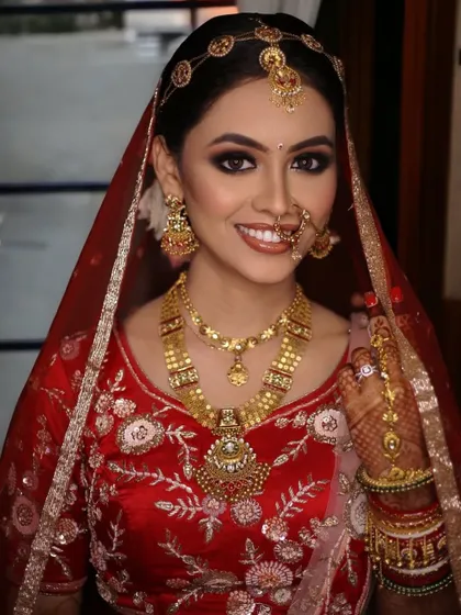 A full portrait of a happy bride. The bold eye makeup is balanced with a natural lip color, and her hair is styled in a traditional bun to support the dupatta and jewelry.