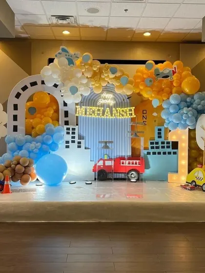 A transportation-themed first birthday party with a city skyline backdrop, road details, and cutouts of a fire truck, police car, and taxi.