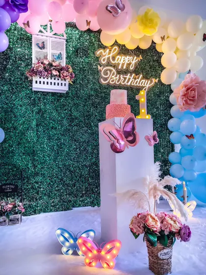 Here, the butterfly theme is set against a lush green hedge wall, creating a beautiful contrast. The neon "Happy Birthday" sign and colorful balloons make the whole scene pop.