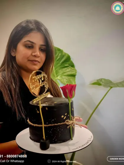 Here I am with one of my elegant creations. This sophisticated black cake is adorned with gold flecks, a single red rose, and a custom "Happy 50th" topper, showcasing my passion for detail.