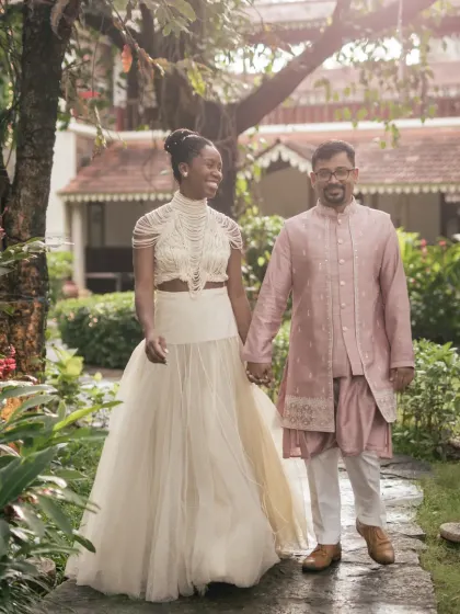 A stylish couple takes a post-ceremony stroll through a garden path. The bride's contemporary two-piece outfit is a perfect example of modern wedding fashion.