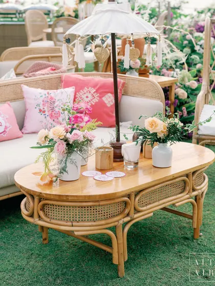A Balinese-inspired coffee table at 'Villa Brissa'. A small umbrella, floral-printed pillows, and rattan furniture create an ambiance that whispers serenity.
