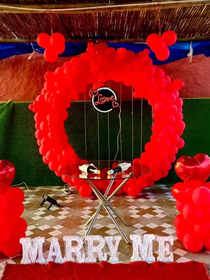 A clear, straight-on shot of the red-themed proposal decor. You can see the details like the heart-shaped foil balloons on top of the pillars and the delicate fairy lights around the "Love" sign.