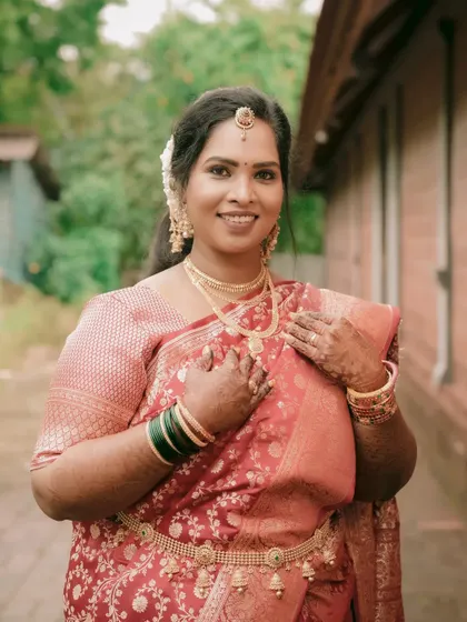 A radiant portrait of a South Indian bride in a beautiful red silk saree. Her smile and traditional gold jewelry, including the waist belt (vaddanam), complete the elegant look.