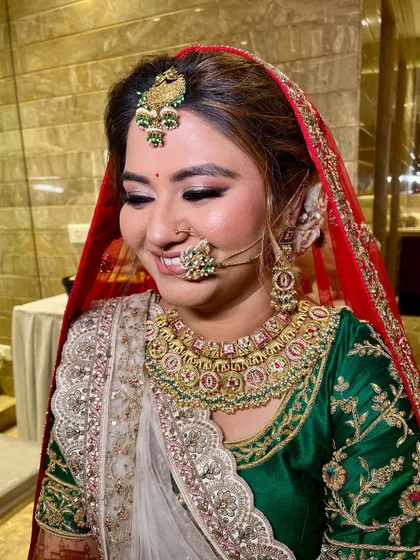 A close-up of a smiling bride. Her makeup features a soft, shimmery eye and a warm pink lip, perfect for her green and red outfit.
