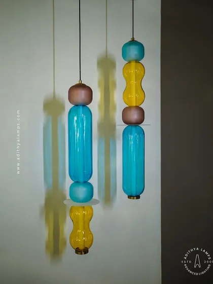 Add a playful pop of color with these kinetic sculpture pendants. Featuring stacked segments of hand-blown glass in teal, amber, and blush, these lights are a fun and artistic addition to any creative space.