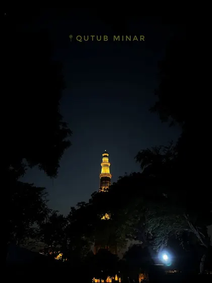 The Qutub Minar seen from a distance at night, framed by the silhouette of trees, creating a mysterious and grand atmosphere.
