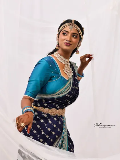 A candid and graceful pose that captures a sense of movement and life. The lighting beautifully highlights the texture of the saree and the glow of the makeup.