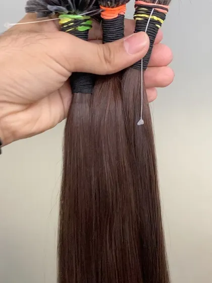A hand holding several bundles of our brown I-Tip extensions, demonstrating their thickness and smooth texture. We provide high-quality hair for a luxurious finish.