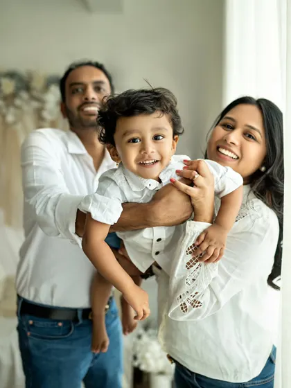 A family portrait filled with bright smiles and natural light. The little boy is the center of attention, held lovingly by his parents.