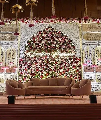 A full view of the stage, featuring a massive floral backdrop in an arched shape, with a custom hashtag. The design uses traditional motifs with a modern, clean execution.