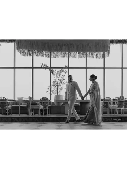 A wide, black and white shot of a couple walking hand-in-hand in a modern, stylish venue, creating a sense of quiet elegance.