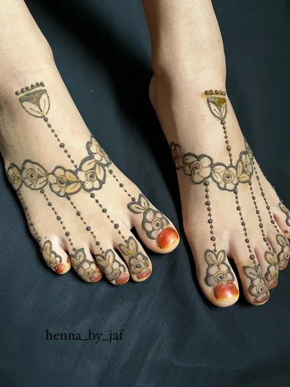 A delicate and symmetrical henna design for the feet. This pattern resembles a traditional anklet, with floral chains draping beautifully over the top of the feet and toes.