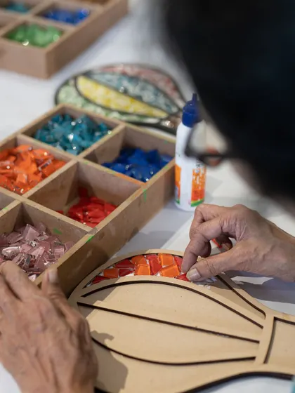 A grandmother focuses on her hot air balloon mosaic, choosing each colorful tile with care. Our mosaic workshops are a fantastic way for different generations to connect and create side-by-side.