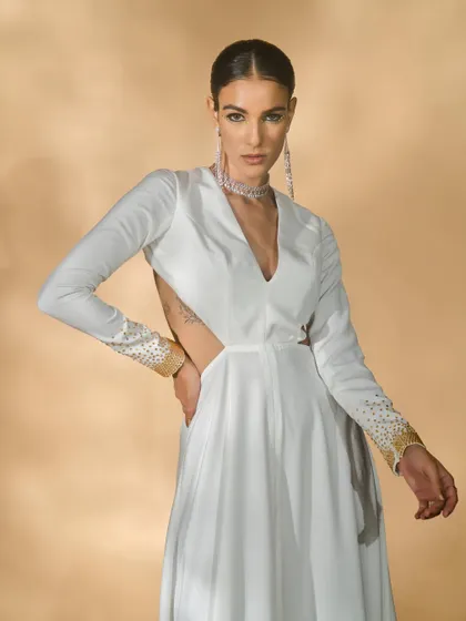 A close-up of a white long-sleeved gown with cut-outs from the 'Ivory Edit'. The pose highlights the sleeve details and the modern silhouette of the dress.